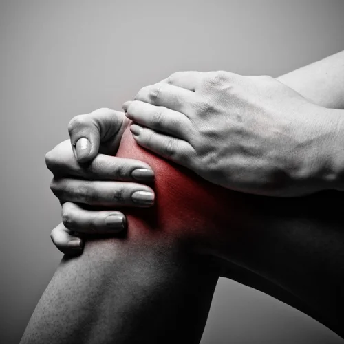 A person holding their knee in pain. Inflammation is indicated with red highlighting