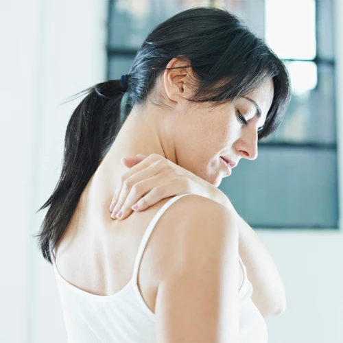 A young woman reaching to hold her shoulder, in pain