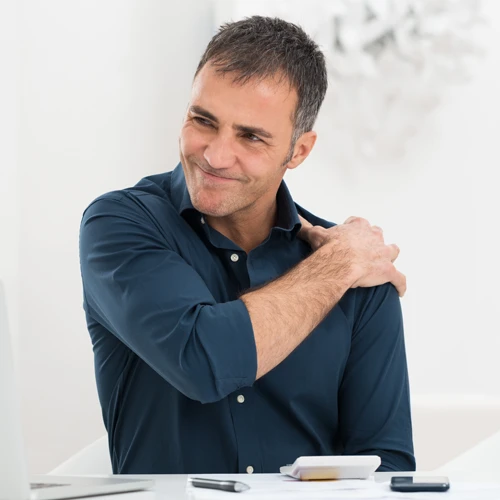 A man sitting at a desk and holding his shoulder in pain